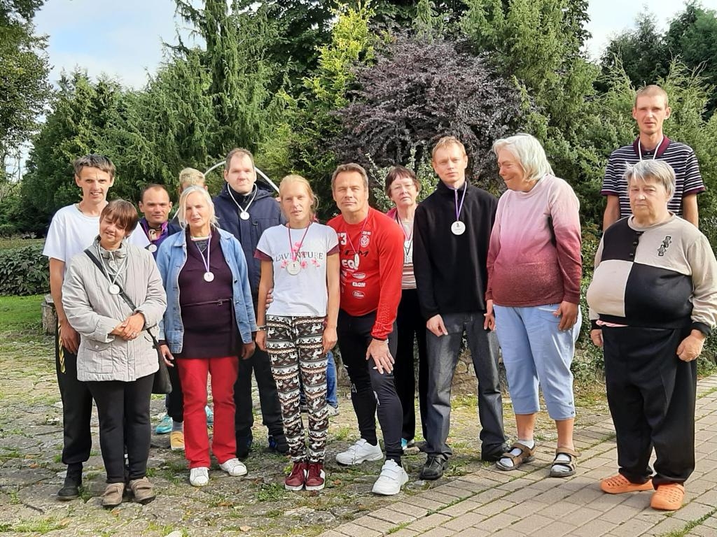 Cilvēkiu grupa s'tav fotogrāfijai, fonā augi