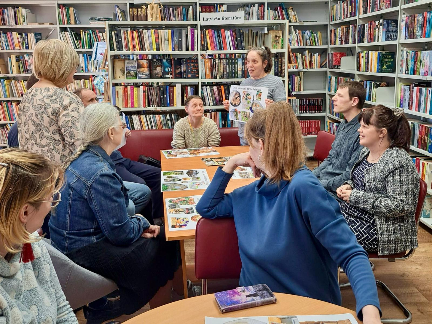 Cilvēki grupas pie galdiem bibliotēkā