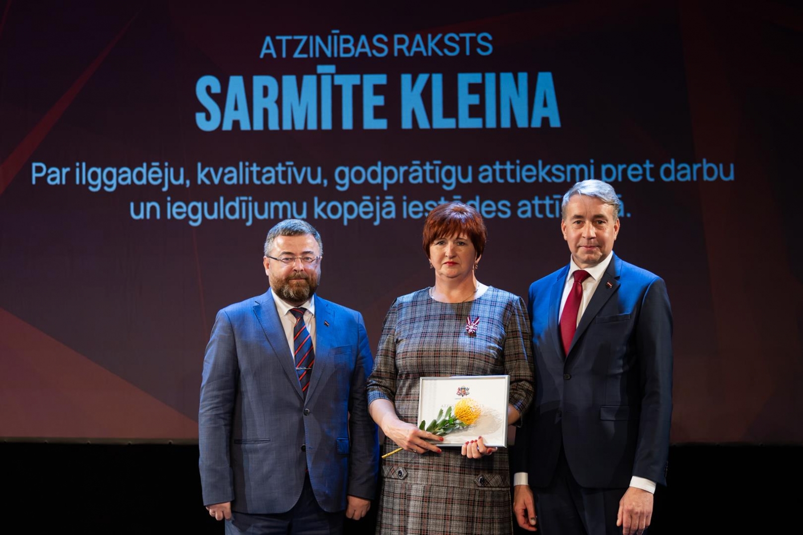 Cilvēki uz skatuves svinīgā pasākumā