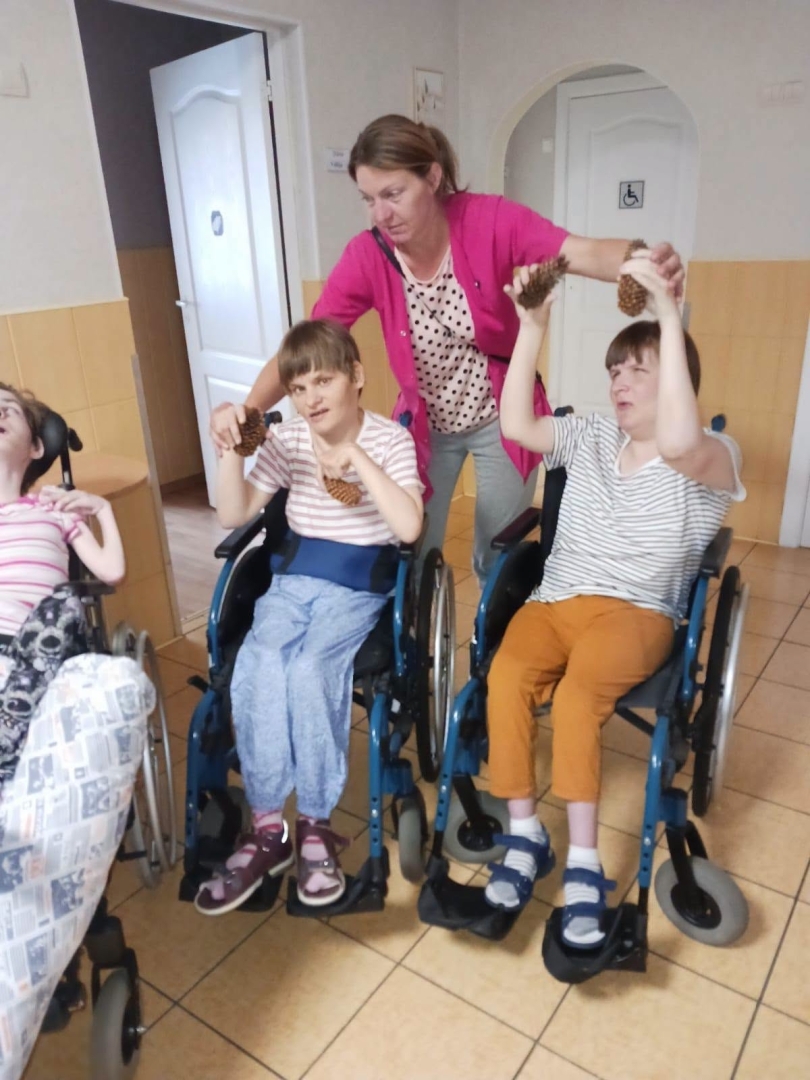 Iedzīvotāji ratiņkrēslā vingro ar darbinieku palīdzību