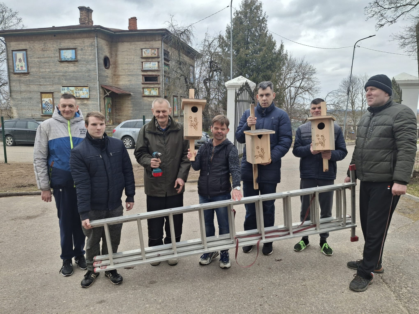 Cilvēku grupa tur rokās pašu gatavotus putnu būrīšus