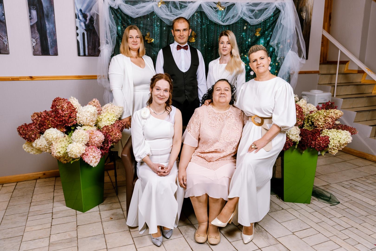 5 sievietis un vīries fotostūrītī, svinīgos tērpos