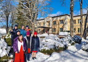 Cilvēku grupa ārā ziemas dienā stāv pie apsnigušiem apstādījumiem