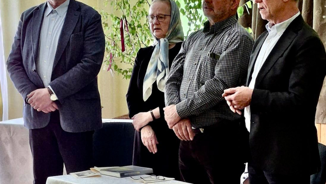 Cilvēki stāv aktu zālē, pie neliela galda