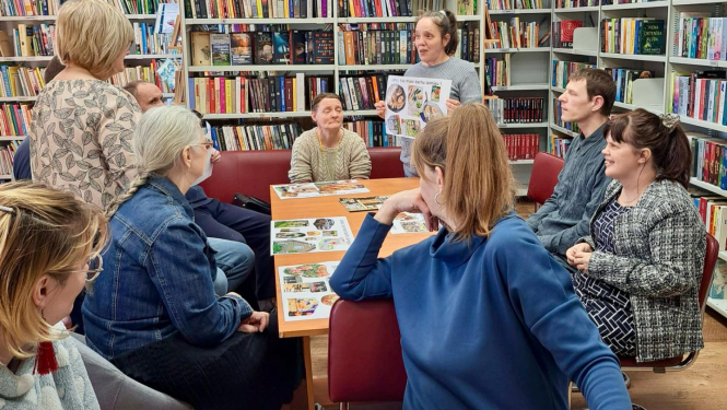 Cilvēki grupas pie galdiem bibliotēkā