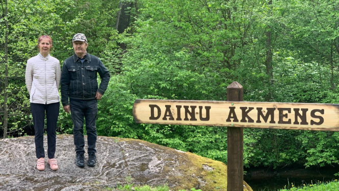 Sieviete un vīrietis stāv uz liela akmens, pie tā zīme Dainu akmens