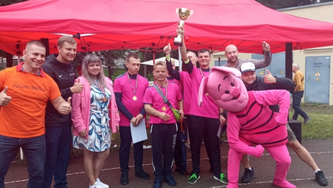 Sportisti stāv pie telts un tura kausu