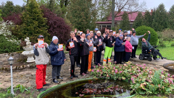 Cilvēku grupa ārā pie strūklakas, tura rokās diplomus