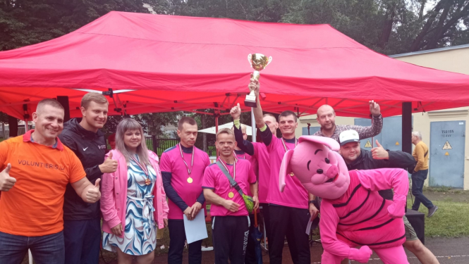 Sportisti stāv pie telts un tura kausu