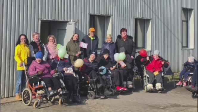 cilvēku grupa pie pelēkas ēkas