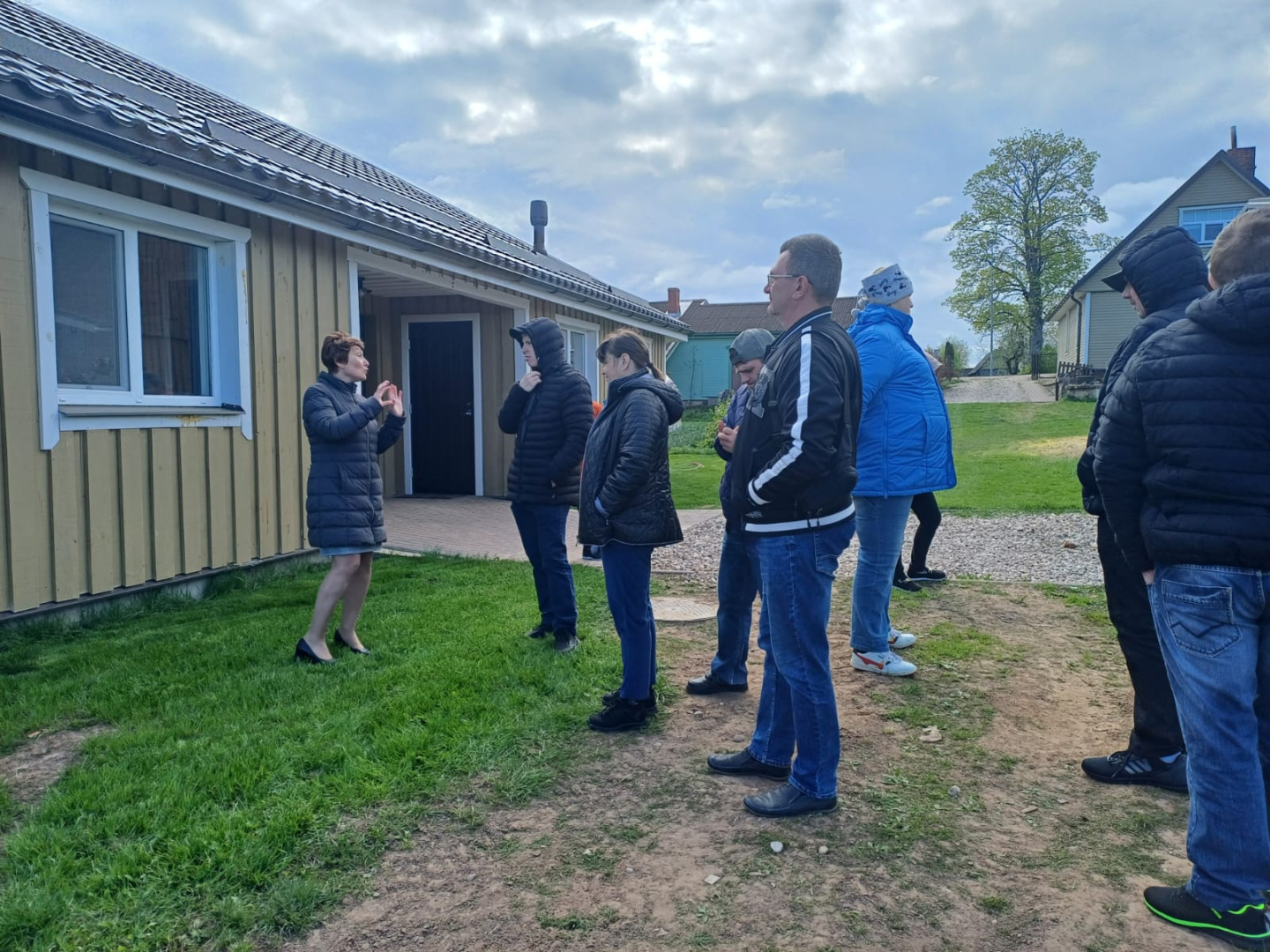 Cilvēku grupa ārā pie vienstāva ēkas