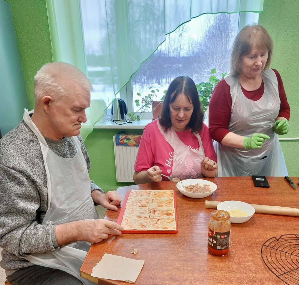 Cilvēki ap galdu gatavo pīrāgus