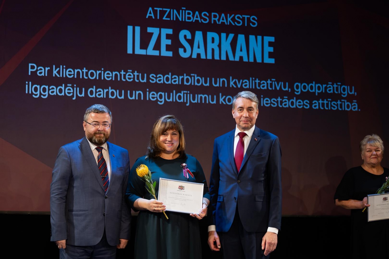 Cilvēki uz skatuves svinīgā pasākumā
