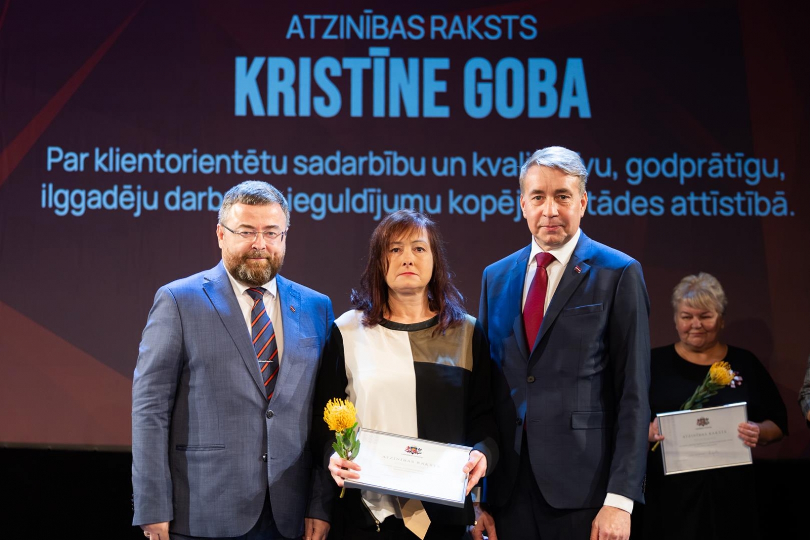 Cilvēki uz skatuves svinīgā pasākumā