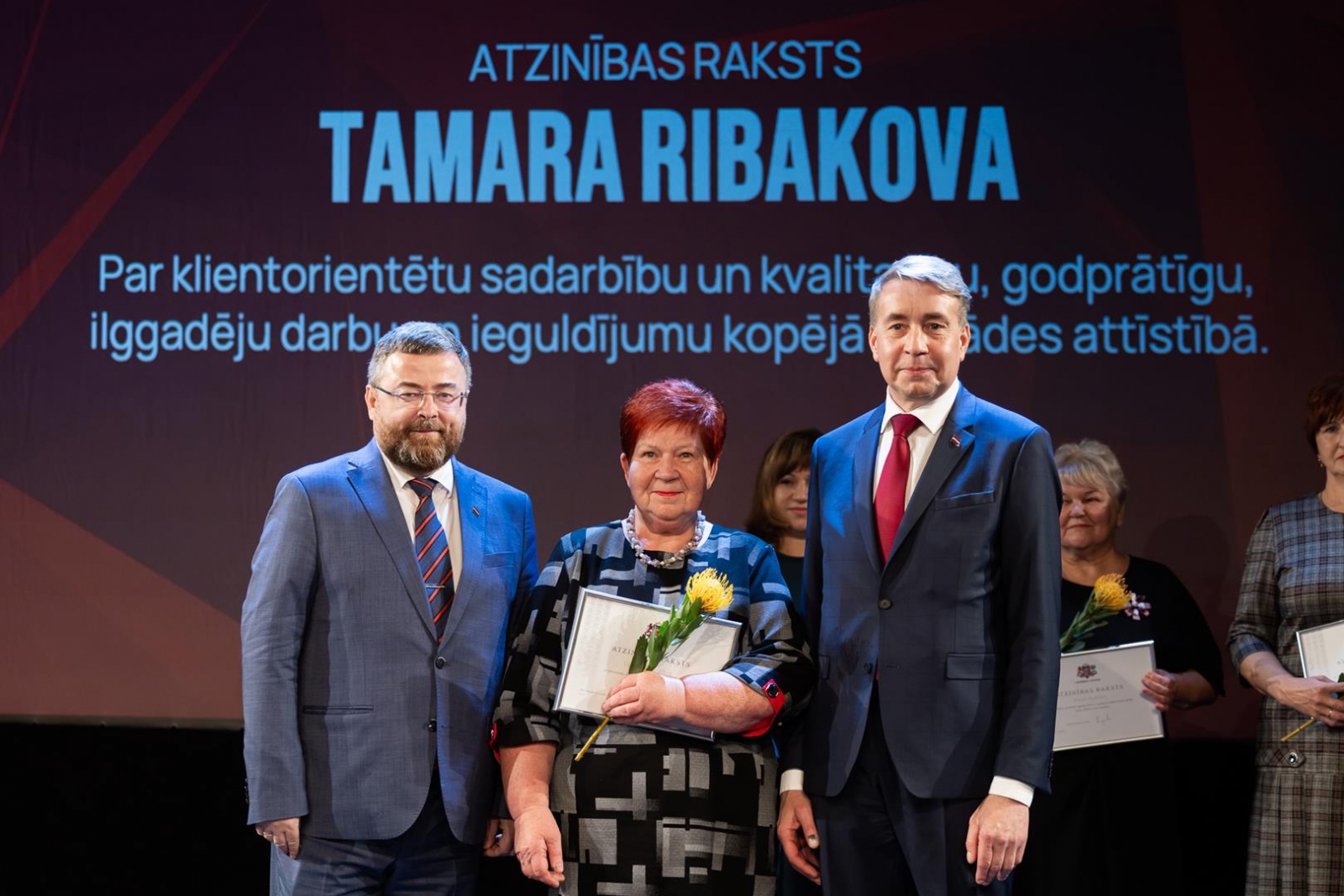 Cilvēki uz skatuves svinīgā pasākumā