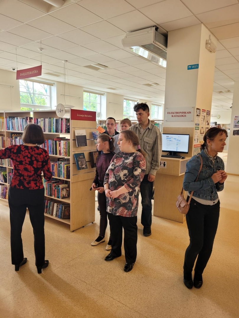 Cilvēku grupa apmeklē bibliotēku