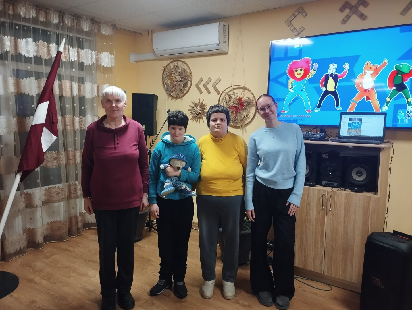 4 cilvēku grupa stāv pie valsts karoga