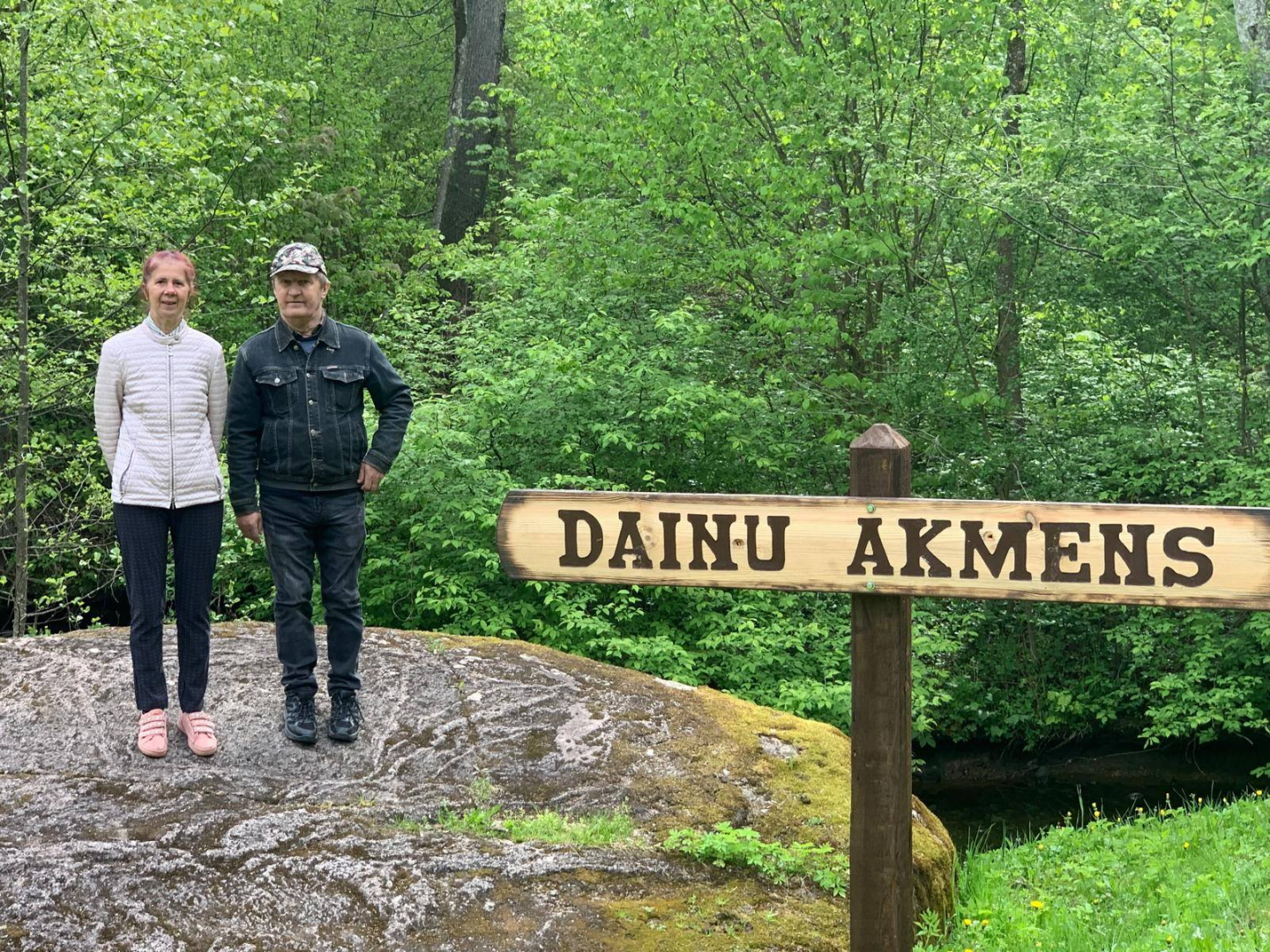Sieviete un vīrietis stāv uz liela akmens, pie tā zīme Dainu akmens