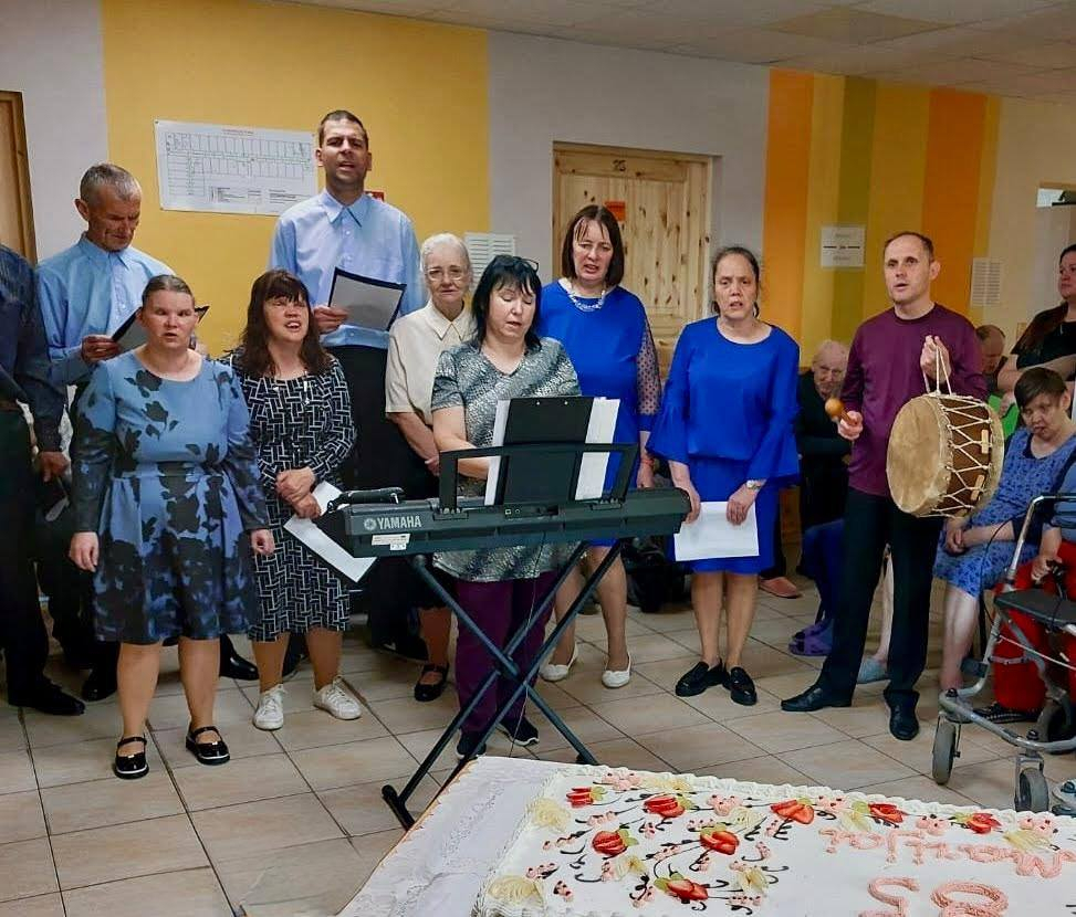 Uzstājas dziedātāju grupa, sieviete speļē sintezatoru