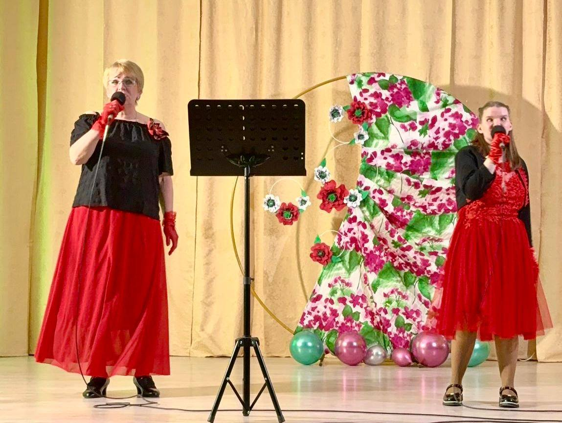 2 sievietes uz skatuves sarkanās kleitās