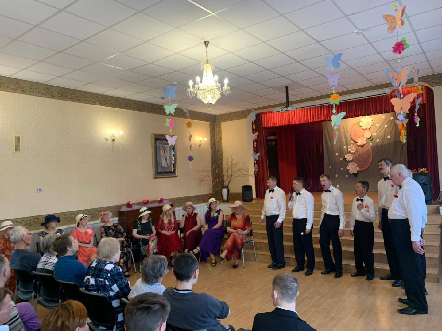 Vīrietis stāv pie skatuves kāpnēm, sieviets sēž zālē