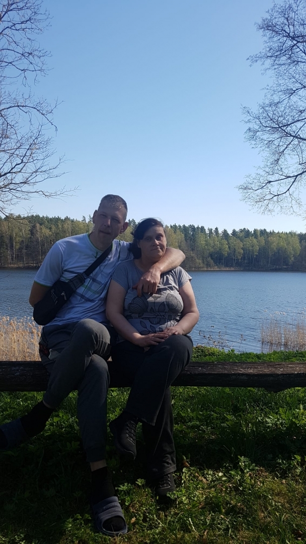 Vīrietis un sieve sēž uz soliņa, fonā ezers