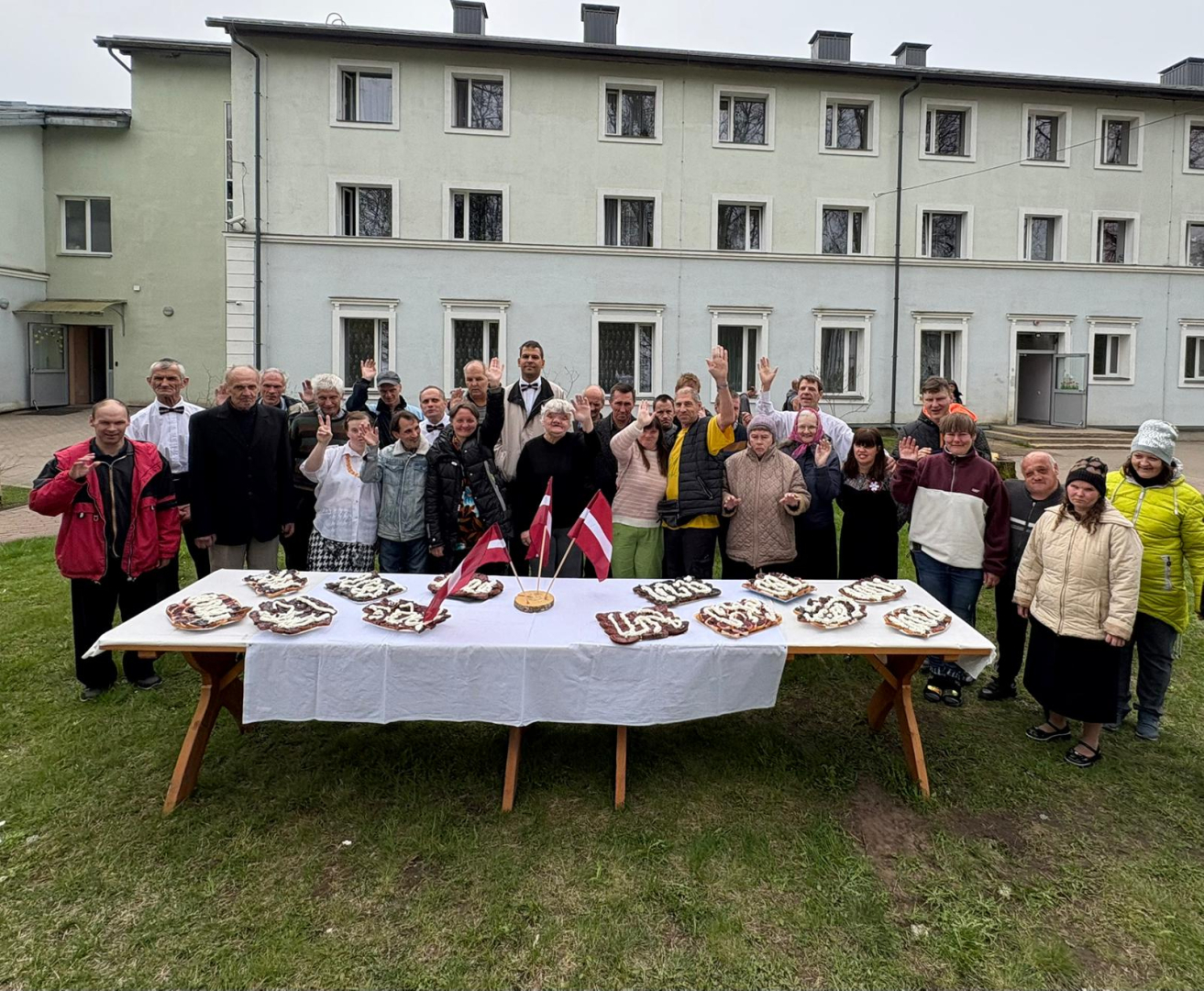 svētku galdas ārā, zālienā, pie  glada cīlvēku grupa