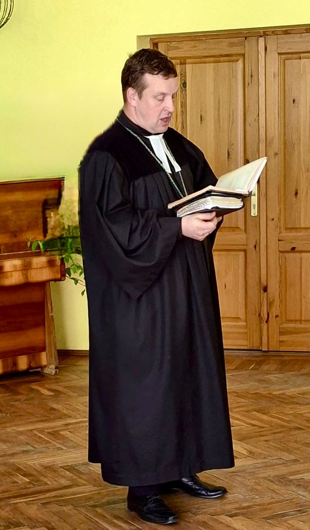 Stāv mācītājs, lasa no grāmatas