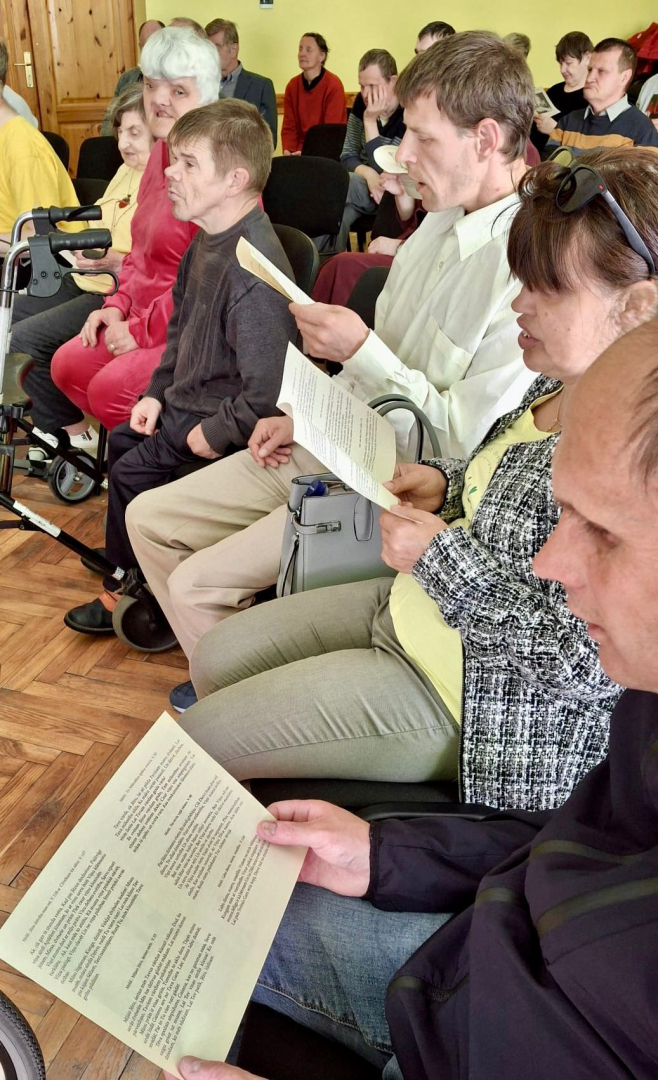 Zālē krēslos sēž cilvēki, rokās grāmatas
