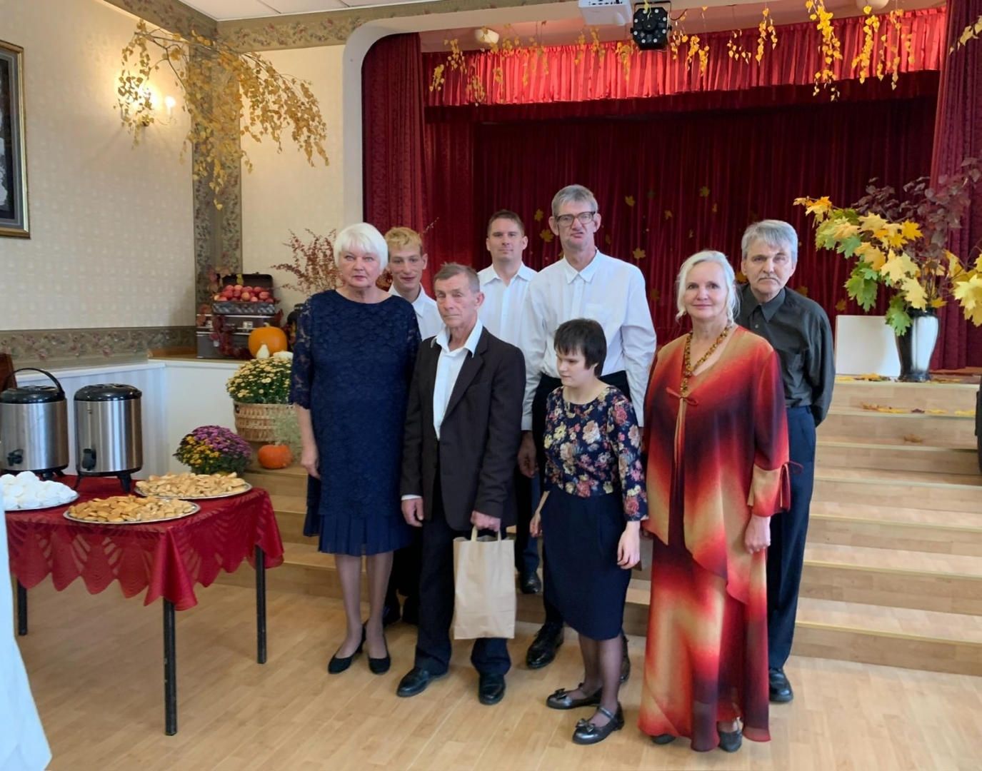 Cilvēku grupa svētku drēbēs stāv pie galda