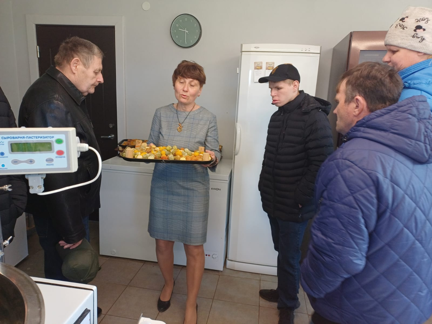 Sieviete tur rokās paplāti ar sieru, apkārt cilvēki