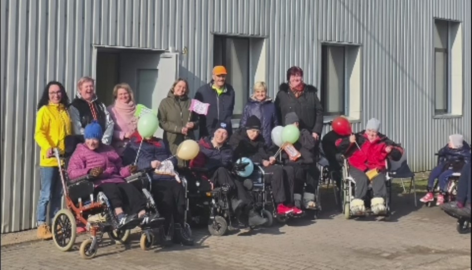 cilvēku grupa pie pelēkas ēkas